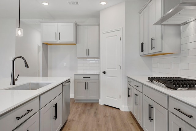 219 Briarwood Dr, Nevada, TX 75173 - kitchen featuring wall chimney range hood, stainless steel appliances, light wood-style flooring, tasteful backsplash, and hanging light fixtures