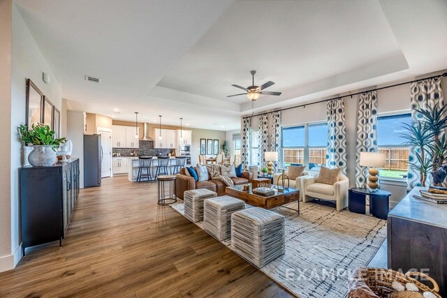 living room featuring wood-type flooring, a tray ceiling, and ceiling fan