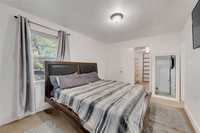 bedroom featuring a textured ceiling, light carpet, and a walk in closet