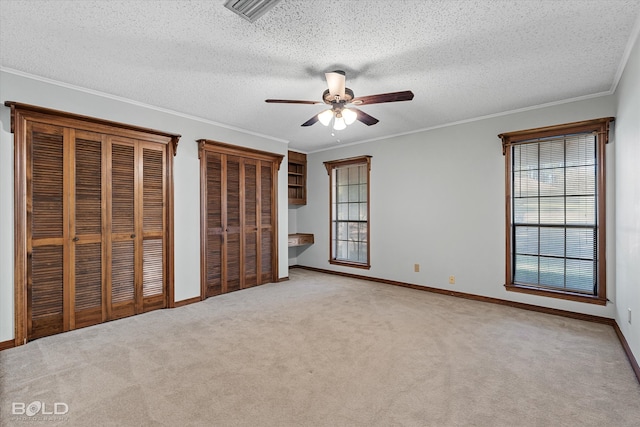 unfurnished bedroom featuring ornamental molding, ceiling fan, a textured ceiling, multiple closets, and light colored carpet