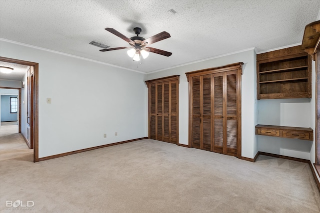 unfurnished bedroom featuring a textured ceiling, multiple closets, light carpet, and ceiling fan