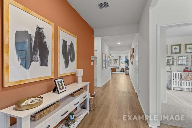 hallway with light wood-style floors, visible vents, and baseboards