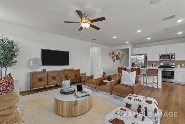 living area with visible vents, baseboards, ceiling fan, light wood-type flooring, and recessed lighting