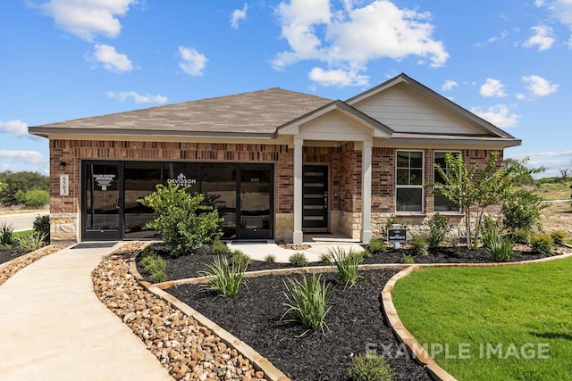 view of front of property featuring a shingled roof, a front yard, and brick siding