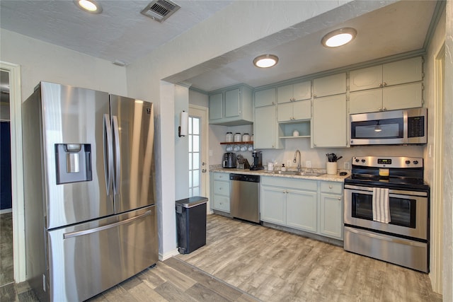 kitchen with sink, appliances with stainless steel finishes, light stone countertops, a textured ceiling, and light wood-type flooring