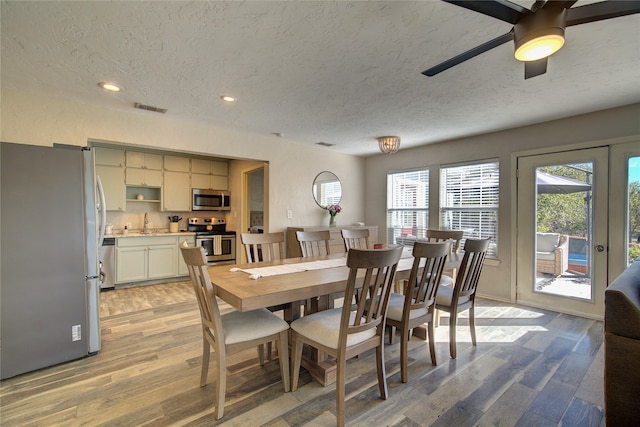 dining area with a textured ceiling, light wood-type flooring, ceiling fan, and sink