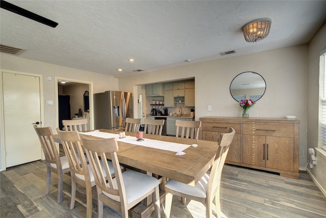 dining area with a textured ceiling, sink, and light hardwood / wood-style flooring