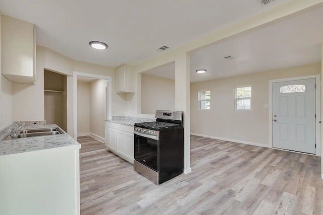 kitchen featuring light stone counters, stainless steel range with gas cooktop, sink, white cabinets, and light hardwood / wood-style flooring