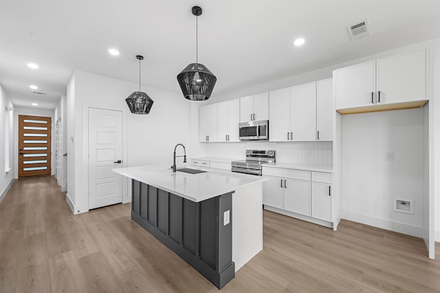 kitchen featuring a center island with sink, sink, pendant lighting, appliances with stainless steel finishes, and white cabinetry