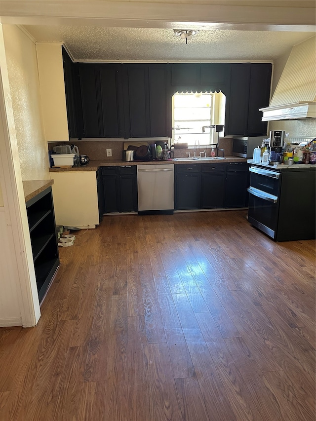 kitchen with stainless steel appliances, a textured ceiling, hardwood / wood-style flooring, sink, and premium range hood