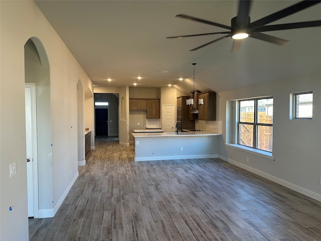 kitchen featuring kitchen peninsula, ceiling fan, backsplash, hanging light fixtures, and dark wood-type flooring