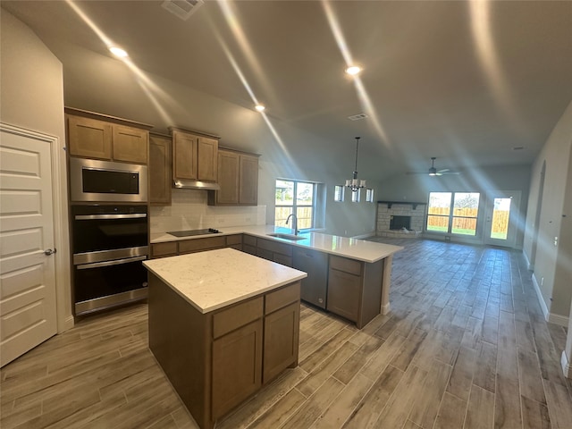 kitchen with a stone fireplace, pendant lighting, vaulted ceiling, hardwood / wood-style flooring, and a center island