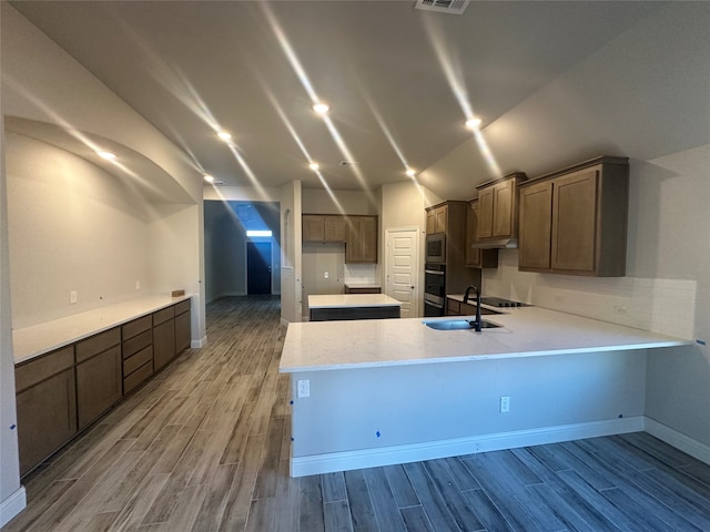 kitchen featuring wood-type flooring, vaulted ceiling, kitchen peninsula, stainless steel microwave, and sink