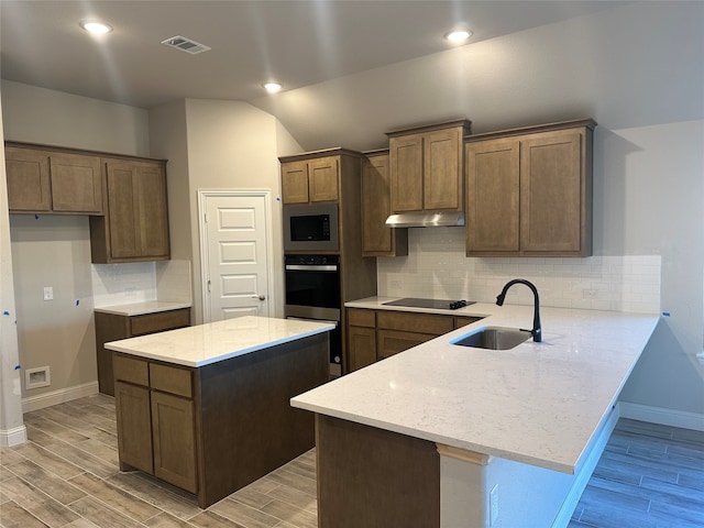 kitchen with light stone counters, stainless steel appliances, sink, light hardwood / wood-style floors, and kitchen peninsula