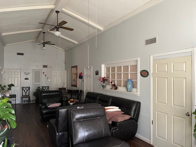 living room with beam ceiling, dark hardwood / wood-style floors, high vaulted ceiling, and ceiling fan