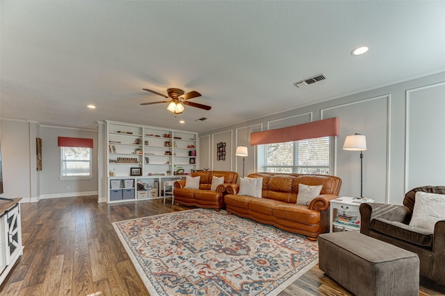 living room with ceiling fan, built in features, dark wood-type flooring, and ornamental molding