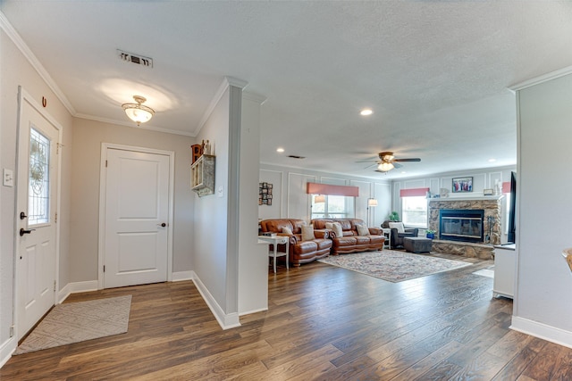 entryway with ceiling fan, dark hardwood / wood-style flooring, crown molding, and a stone fireplace