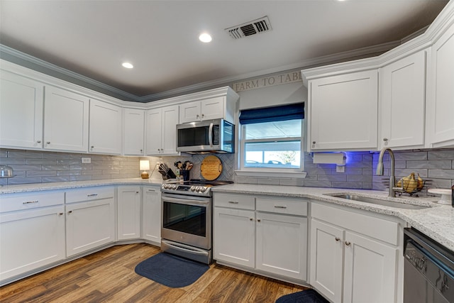 kitchen with white cabinetry, hardwood / wood-style floors, appliances with stainless steel finishes, light stone counters, and sink