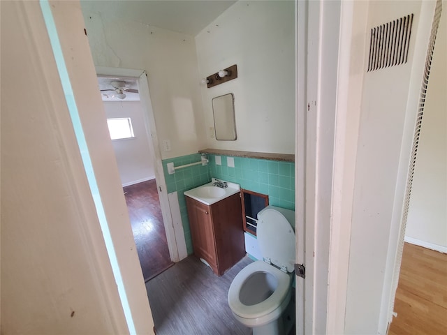 bathroom with tile walls, vanity, hardwood / wood-style floors, toilet, and ceiling fan