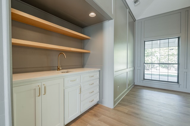 bar featuring white cabinetry, sink, light hardwood / wood-style flooring, and light stone countertops