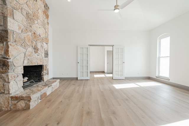 unfurnished living room featuring french doors, ceiling fan, a stone fireplace, and light hardwood / wood-style floors