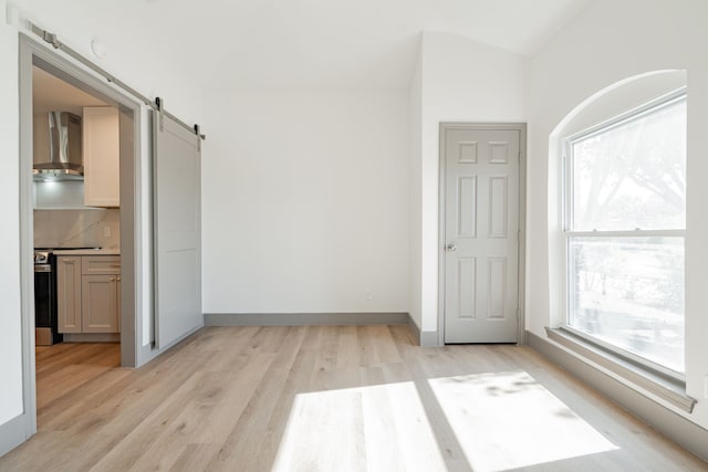 unfurnished room with lofted ceiling, a barn door, and light hardwood / wood-style flooring