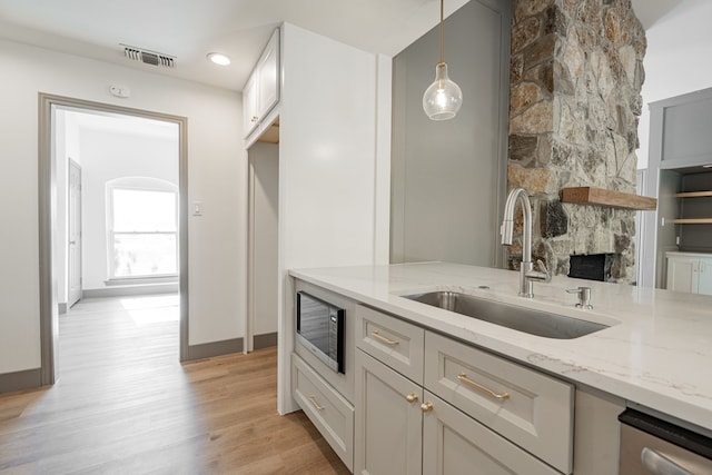 kitchen featuring pendant lighting, sink, stainless steel microwave, a fireplace, and light stone countertops