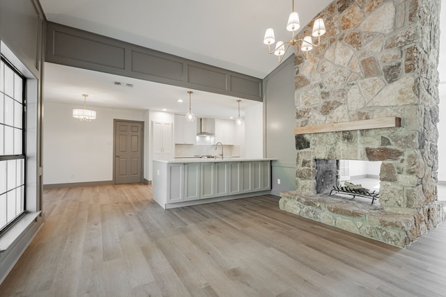 unfurnished living room with an inviting chandelier, a fireplace, sink, and light hardwood / wood-style flooring