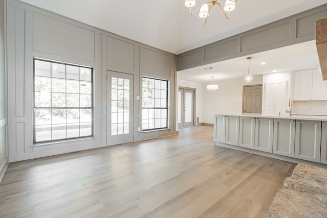 unfurnished living room featuring sink, a towering ceiling, light hardwood / wood-style flooring, and a chandelier