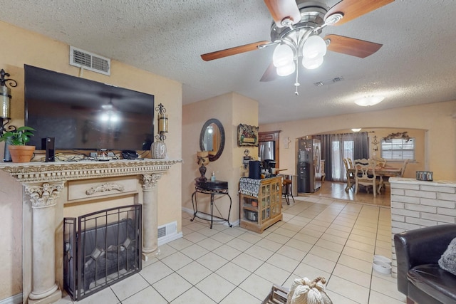 tiled living room featuring a brick fireplace, ceiling fan, and a textured ceiling