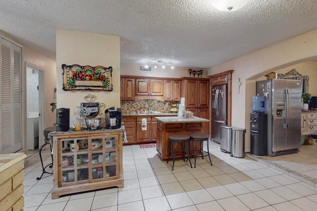 kitchen with stainless steel refrigerator with ice dispenser, a textured ceiling, a kitchen breakfast bar, and a center island