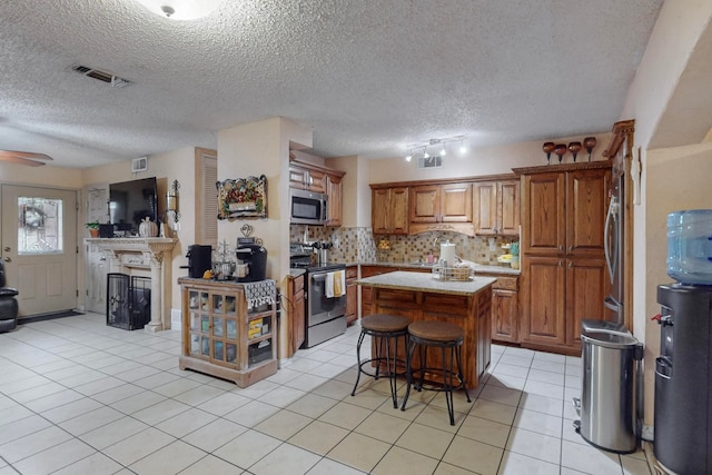 kitchen featuring a center island, a textured ceiling, light tile patterned floors, a breakfast bar, and appliances with stainless steel finishes