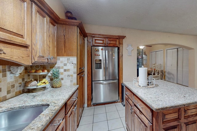 kitchen featuring light stone counters, a textured ceiling, tasteful backsplash, stainless steel fridge with ice dispenser, and light tile patterned floors