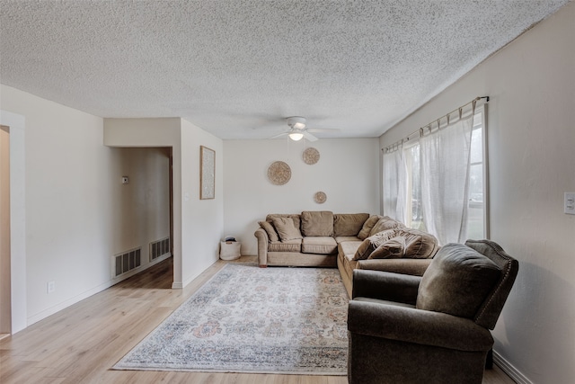 living room with a textured ceiling, ceiling fan, and light hardwood / wood-style flooring