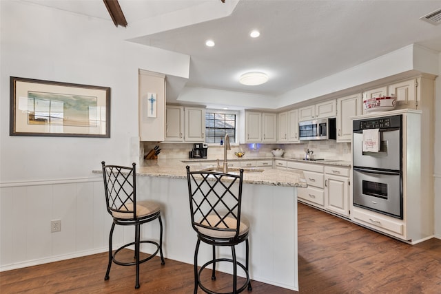 kitchen with kitchen peninsula, dark hardwood / wood-style floors, a breakfast bar, and appliances with stainless steel finishes