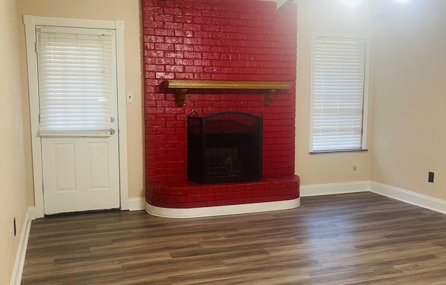 unfurnished living room featuring a brick fireplace and dark hardwood / wood-style floors