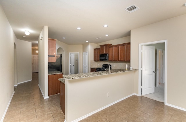 kitchen featuring kitchen peninsula, light stone counters, sink, black appliances, and light tile patterned flooring