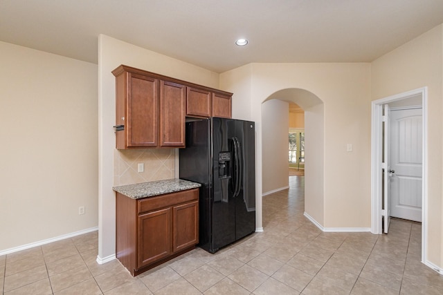 kitchen featuring decorative backsplash, black fridge, light stone countertops, and light tile patterned floors