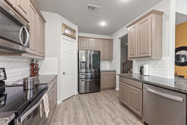 kitchen with dark stone counters, light hardwood / wood-style flooring, a textured ceiling, backsplash, and appliances with stainless steel finishes