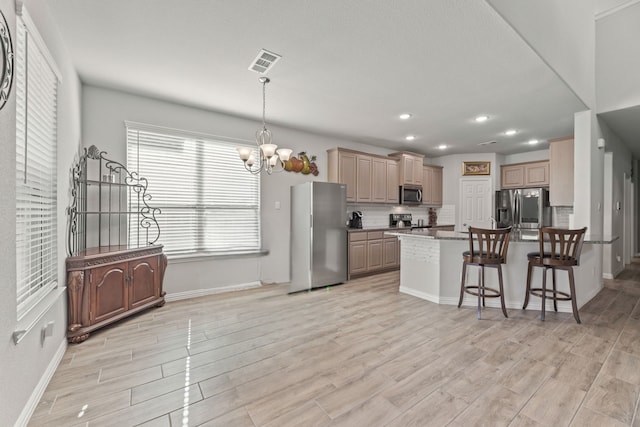 kitchen featuring stainless steel appliances, backsplash, a notable chandelier, a breakfast bar area, and light hardwood / wood-style flooring