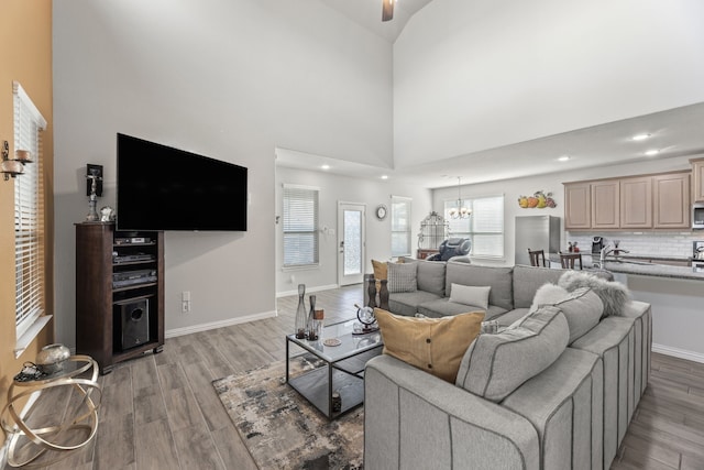 living room with high vaulted ceiling, light hardwood / wood-style floors, and ceiling fan with notable chandelier