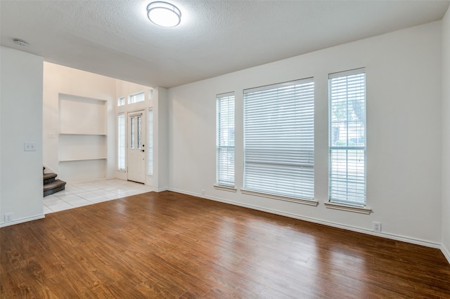 unfurnished room featuring built in features, a textured ceiling, and light hardwood / wood-style flooring