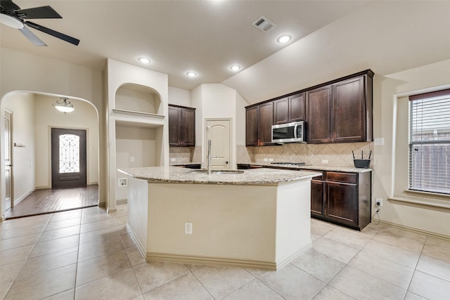 kitchen with appliances with stainless steel finishes, sink, light stone countertops, and a kitchen island with sink