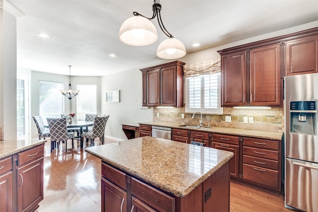 kitchen featuring stainless steel appliances, light hardwood / wood-style floors, sink, decorative light fixtures, and a center island