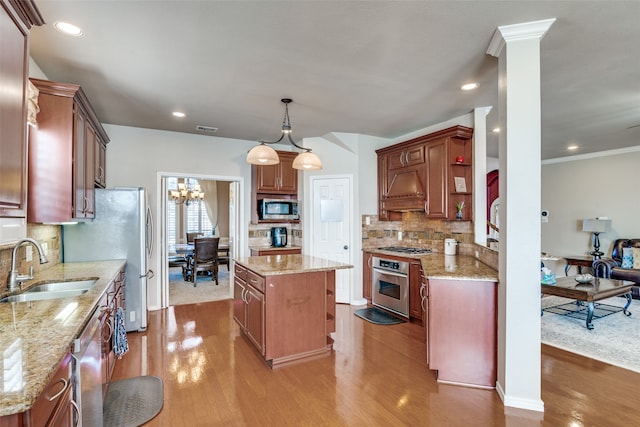 kitchen featuring stainless steel appliances, a kitchen island, decorative light fixtures, sink, and light hardwood / wood-style flooring