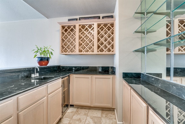 bar with dark stone countertops, beverage cooler, sink, and a textured ceiling