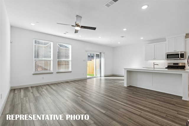 kitchen with white cabinetry, appliances with stainless steel finishes, decorative backsplash, hardwood / wood-style floors, and ceiling fan