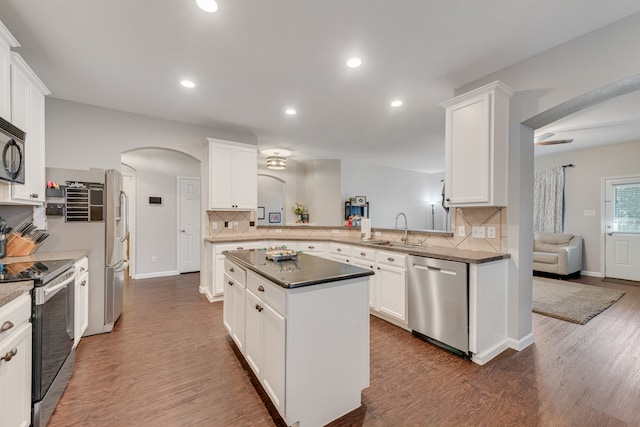 kitchen with kitchen peninsula, appliances with stainless steel finishes, dark wood-type flooring, sink, and white cabinets