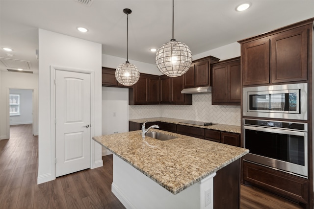 kitchen featuring light stone counters, appliances with stainless steel finishes, pendant lighting, an island with sink, and dark wood-type flooring