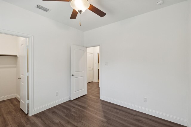 unfurnished bedroom with dark wood-type flooring, ceiling fan, a closet, and a spacious closet